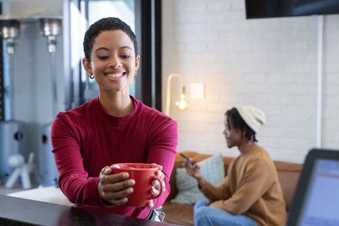 African american woman smiling holding red mug in cozy coworking lounge with friend