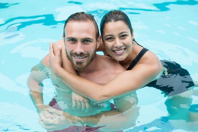 Couple enjoying time together in a swimming pool, embracing and smiling at the camera. Ideal for use in advertisements for summer vacations, swimwear, poolside activities, and romantic getaways. Perfect for promoting leisure and relaxation products or services.