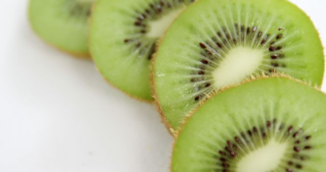 This vibrant image features a close-up of fresh kiwi slices set against a clean white background. Perfect for health and wellness blogs, cooking websites, advertising for healthy diets and tropical fruit promotions. The striking green color and detailed texture can be used to highlight natural foods and fresh produce.