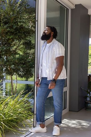 African man standing at sliding glass door enjoying garden sunlight wearing wristwatch