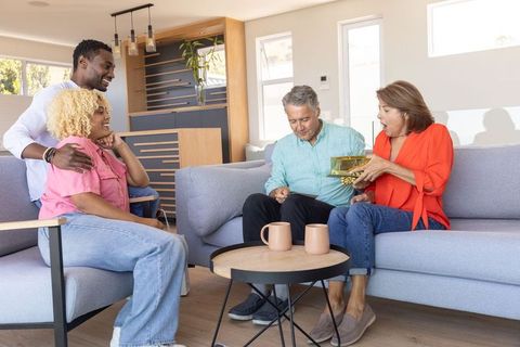 Multigenerational diverse couples exchanging gold-wrapped gift in cozy modern living room