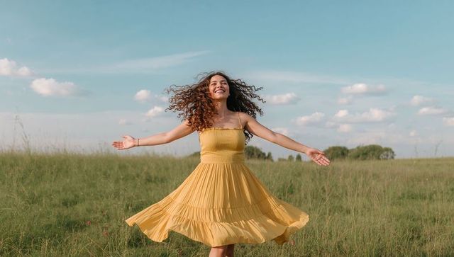 Hispanic woman twirling in yellow sundress on sunlit meadow, joyful summer breeze