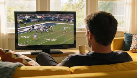 Man watching football on tv from sunlit living room sofa, relaxing game day at home