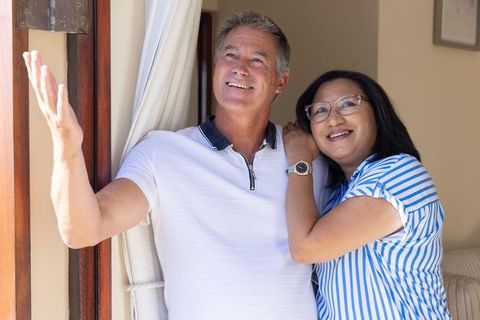 Mature couple smiling and looking outside from doorway, enjoying sunny home moment