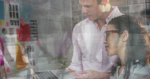 Colleagues Collaborating Over Laptop Through Reflective Glass in Modern Office Workspace