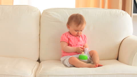 Adorable Baby Sitting on Sofa with Bottle