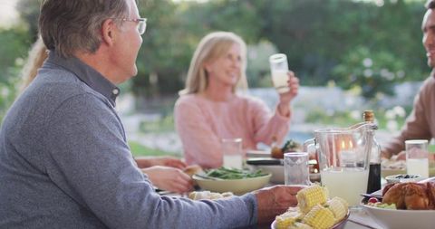 Mature man grabbing corn at outdoor family dinner gathering, casual backyard meal