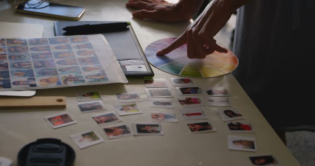 Person is selectively choosing from a colorful palette while various printed portraits are scattered on a desk, likely deciding on color schemes. This can be used for concepts related to creativity, designing, organizing, planning, or a creative workspace.