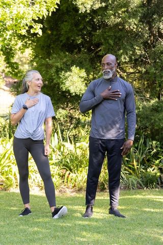 Middle-aged woman and senior african american man practicing breathwork in sunlit garden