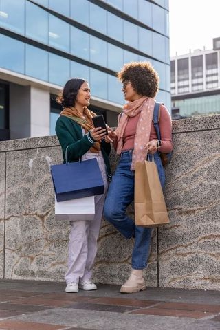 Multicultural friends shopping and chatting with smartphone in modern city plaza