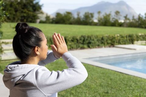Young woman practicing meditation poolside in sunny backyard with mountain view