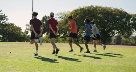 Male teammates jogging high-knee warmup on grass during outdoor team training session