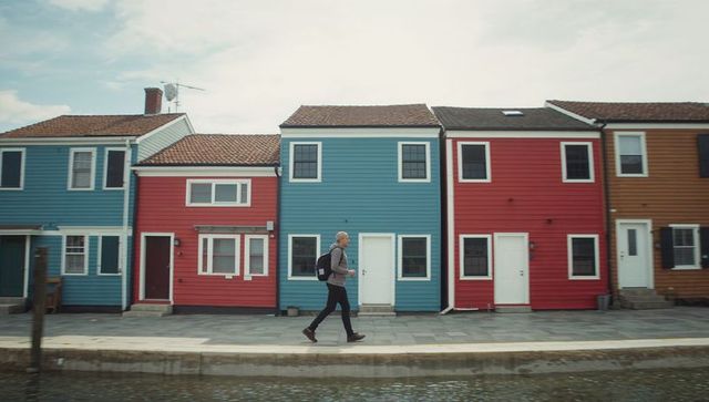 Man walking along canal past colorful waterfront houses carrying backpack