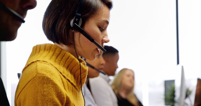 Close up of a multi ethnic team of customer service executives talking on headset at desk in office. They are typing on their computer while speaking with clients.