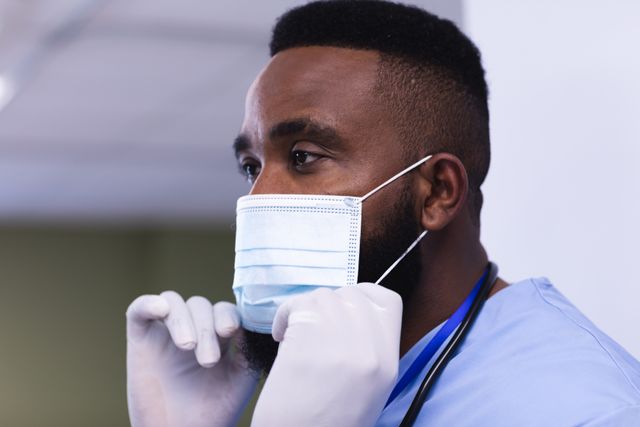 African american male doctor adjusting his face mask in hospital ward. Medical services, hospital and healthcare concept.