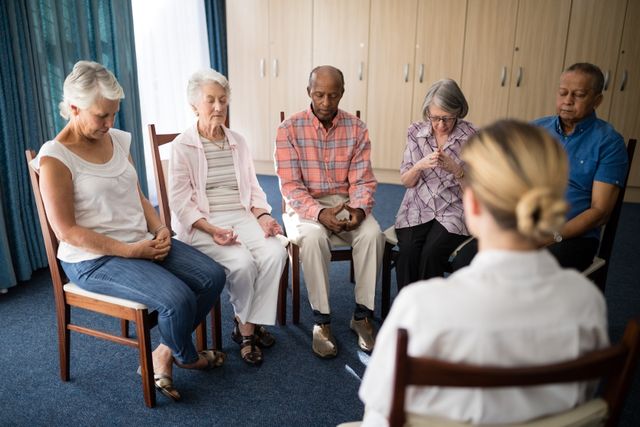 Elderly individuals sitting in a circle, engaging in a meditation session led by a female doctor in a retirement home. This image can be used for promoting senior wellness programs, mental health awareness, retirement home activities, and healthcare services for the elderly.