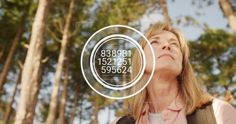 Mature woman hiking through pine forest with augmented reality HUD overlay, looking up