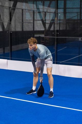 Young male padel player bending forward preparing serve on blue indoor court