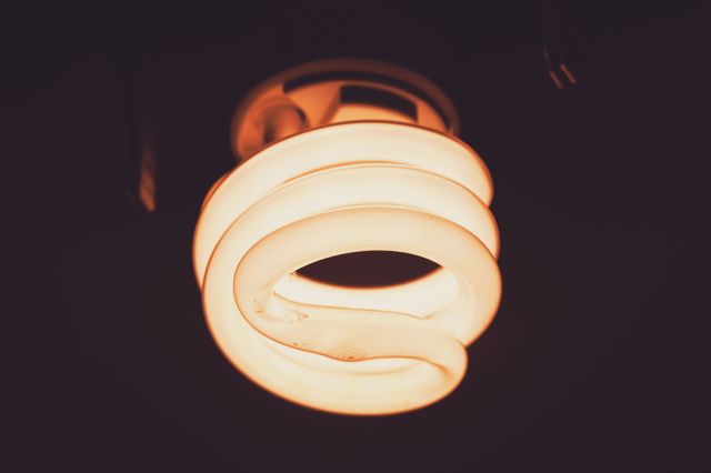Close-up view of a glowing spiral light bulb against a dark background, emitting warm light. Useful for themes related to energy efficiency, sustainable lighting solutions, home decor, and electric technology.