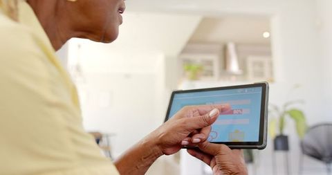 Senior woman monitoring home energy usage on tablet indoors