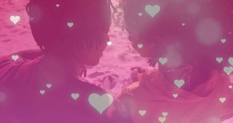 Romantic biracial couple embracing on beach with falling hearts