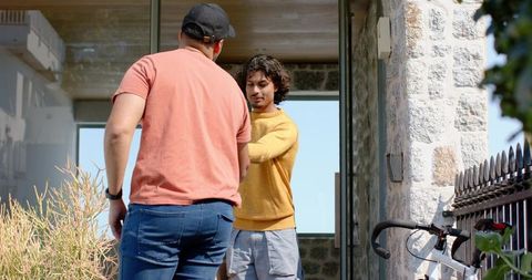 Two men exchanging package at stone house entrance standing by bicycle and succulents