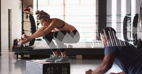 Female athlete balancing on 20-inch plyo box while trainer coaching plyometric jump in gym