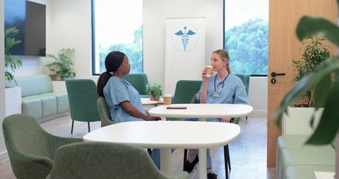 Female healthcare workers sipping coffee and chatting in staff lounge with stethoscope
