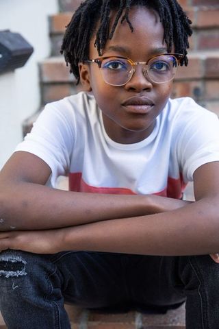 Young Boy with Glasses Sitting on Brick Stairs, Urban Background