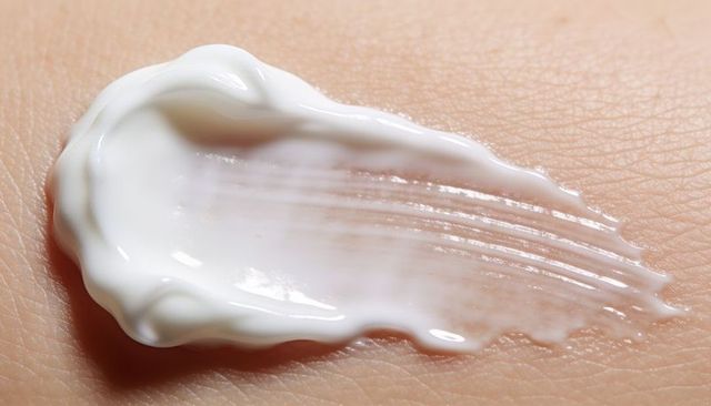 Glossy white cream spreading across skin macro with streak texture and specular highlight