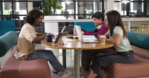 College Students Collaborating at Round Table in Modern Campus Study Lounge with Laptops and Coffee