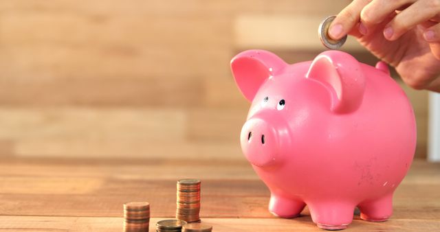 A person saves money by depositing a coin into a piggy bank, highlighting wealth accumulation. - Download Free Stock Photos Pikwizard.com