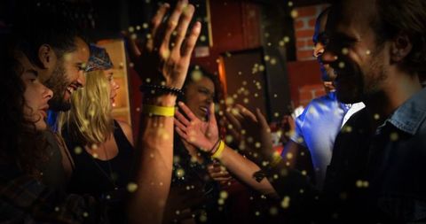 Laughing friends raising hands and chatting in energetic nightclub crowd with wristbands
