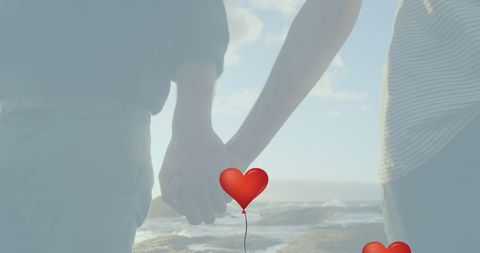 Couple Holding Hands by Sea with Red Heart Balloon