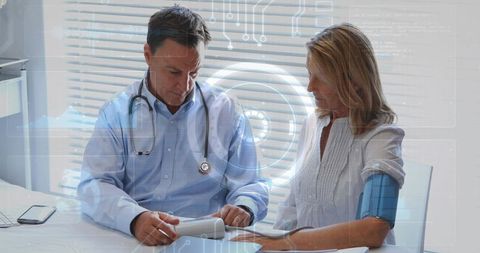 Doctor checking blood pressure with digital cuff while patient reviewing monitor results