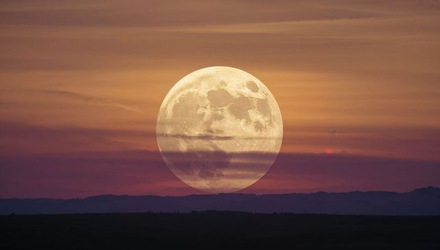 Rising full moon dominating low horizon at twilight with silhouetted mountain ridge