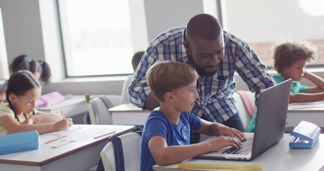 Teacher assisting young boy with laptop in a bright classroom, emphasizing learning and education. Ideal for use in educational content, technology in schools, tutoring services, and promoting modern classrooms.