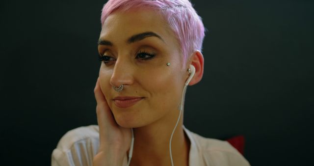 Young Caucasian woman listens to music on earphones, with copy space. Her pink hair and nose piercing give a modern, trendy vibe at home.