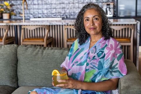 Middle-aged african american woman relaxing on sofa with citrus drink in colorful wrap