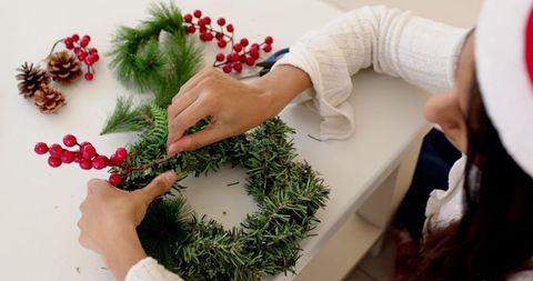Woman crafting pine wreath with red berries for festive home decor