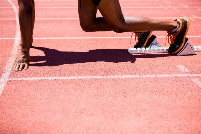 This image captures a determined athlete on a starting block, ready to sprint on a track. Ideal for use in sports-related content, fitness promotions, motivational posters, and articles about athletic training and competition.