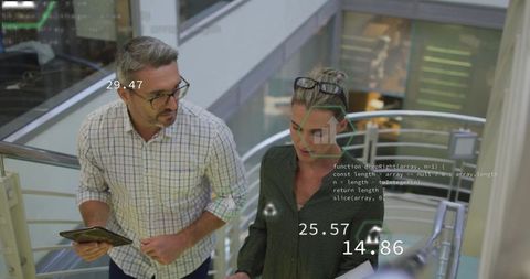 Business colleagues walking atrium reviewing tablet and documents with data overlays