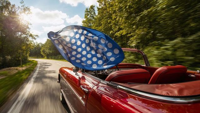 Red convertible driving fast on curving tree-lined road with blue polka-dot canopy