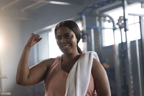 African american woman flexing arm and smiling after workout, celebrating strength with towel