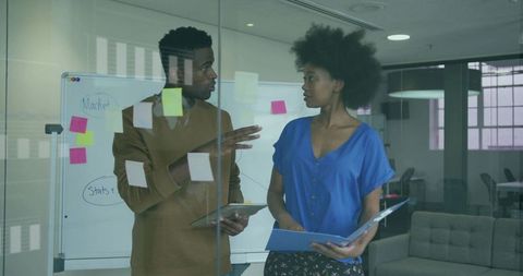 Collaborating in modern glass office using sticky notes, whiteboard, tablet and folder