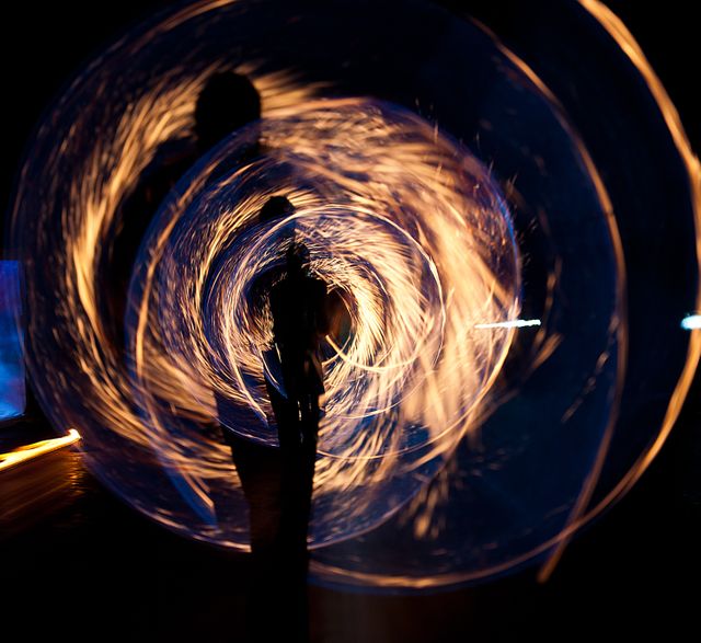 This abstract artwork captures a silhouette standing against swirling light trails, creating a dynamic and captivating effect. The long exposure technique used to capture the movement of the lights produces an ethereal quality, making it perfect for use in art projects, websites focused on creativity, event posters, or as a striking desktop background.