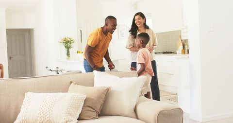 Laughing family interacting in bright modern kitchen with cozy neutral-tone living room lifestyle sc