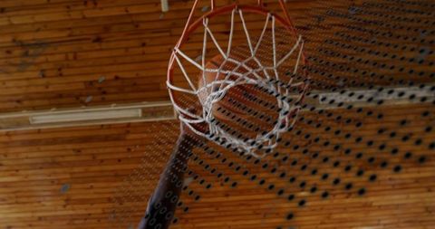 Low-angle basketball hoop hanging under wooden gym ceiling with orange rim and white net