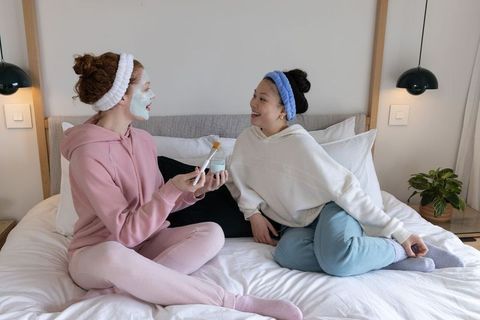 Two friends sharing skincare and facial mask during cozy minimalist bedroom spa night
