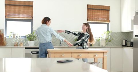 Friends dancing in bright modern kitchen holding hands around wooden island